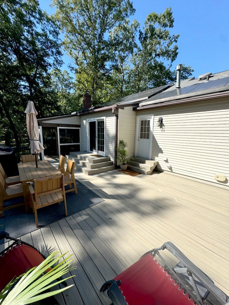 A wooden deck with patio furniture and a house with a door and sliding glass doors on a sunny day.
