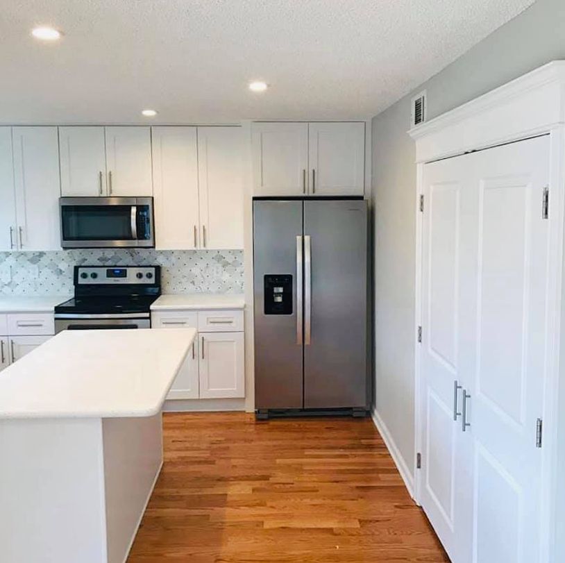 A kitchen with white cabinets , a stainless steel refrigerator , a stove , and a microwave.