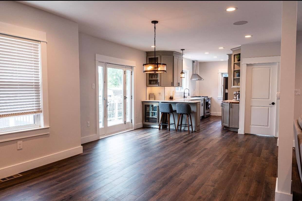 A living room with hardwood floors and a kitchen in the background.