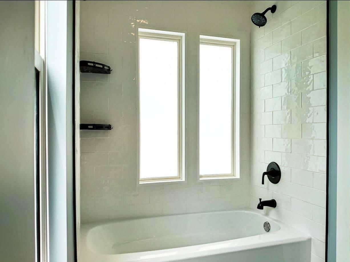 A bathroom with a bathtub , shower , and two windows.