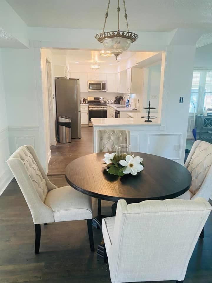A dining room with a round table and chairs and a kitchen in the background.