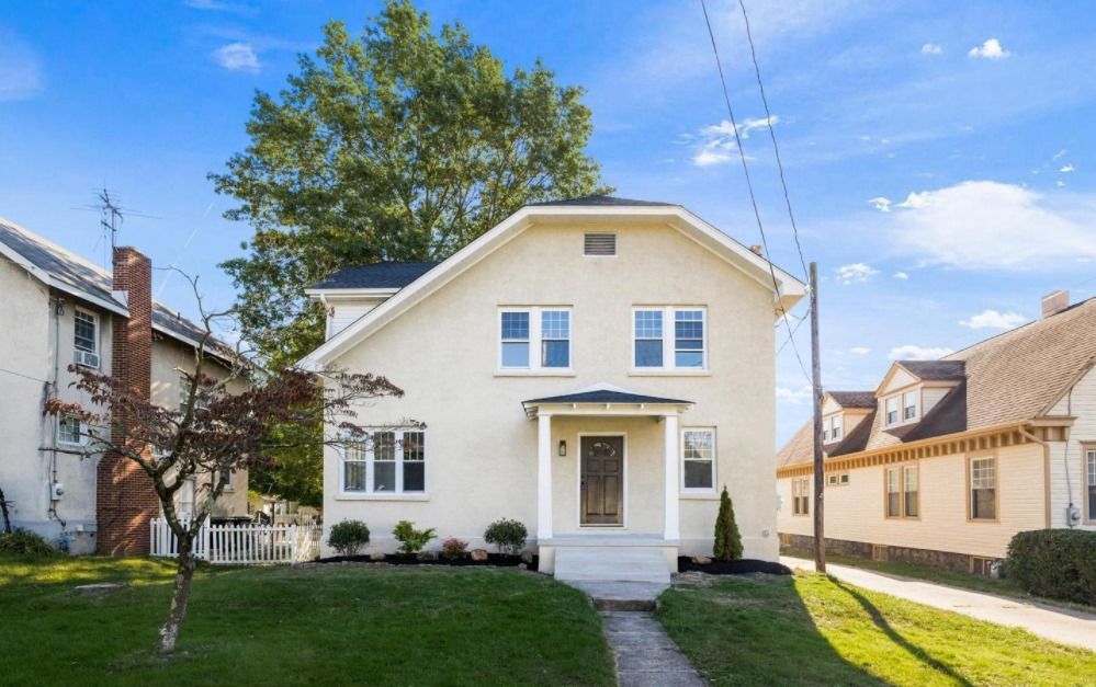 A white house with a porch and a tree in front of it.