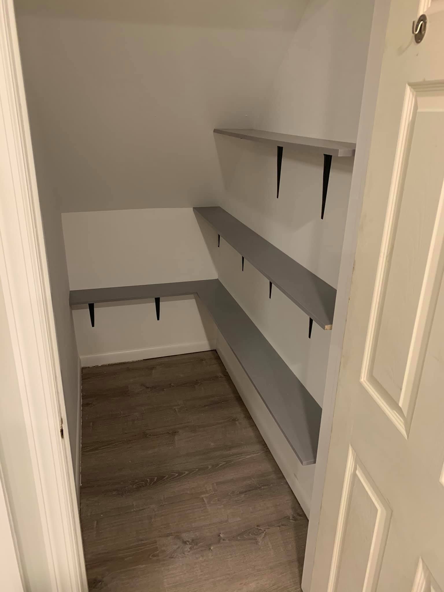A small closet with gray shelves and a wooden floor.