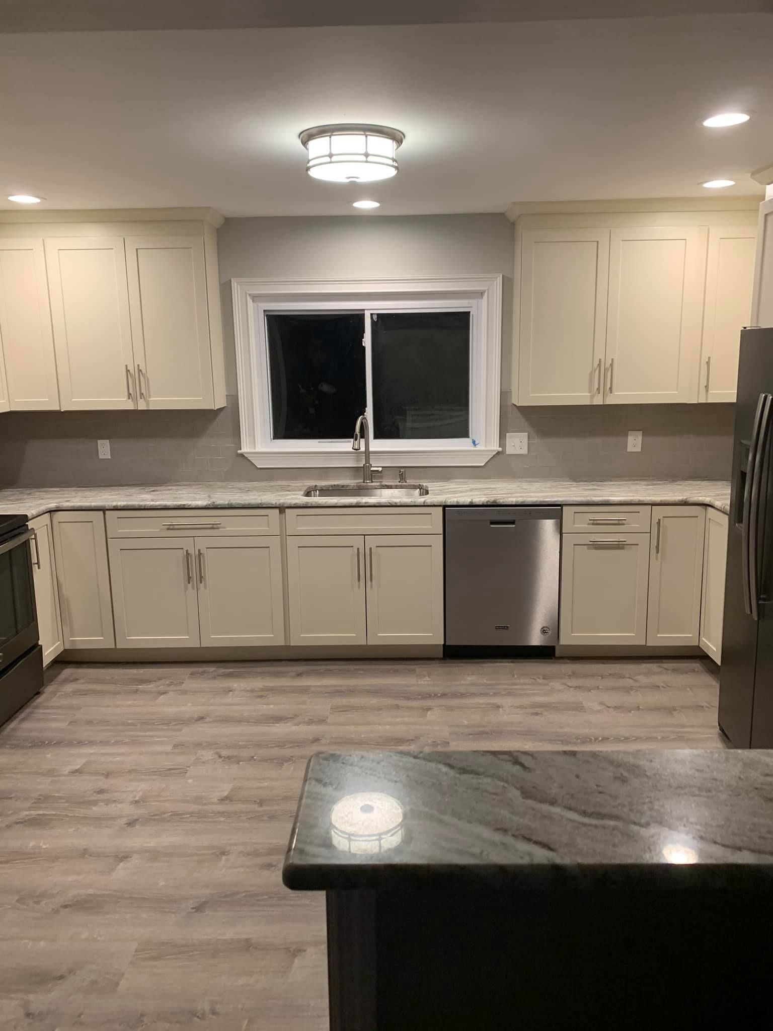 A kitchen with white cabinets , stainless steel appliances , granite counter tops and a large window.