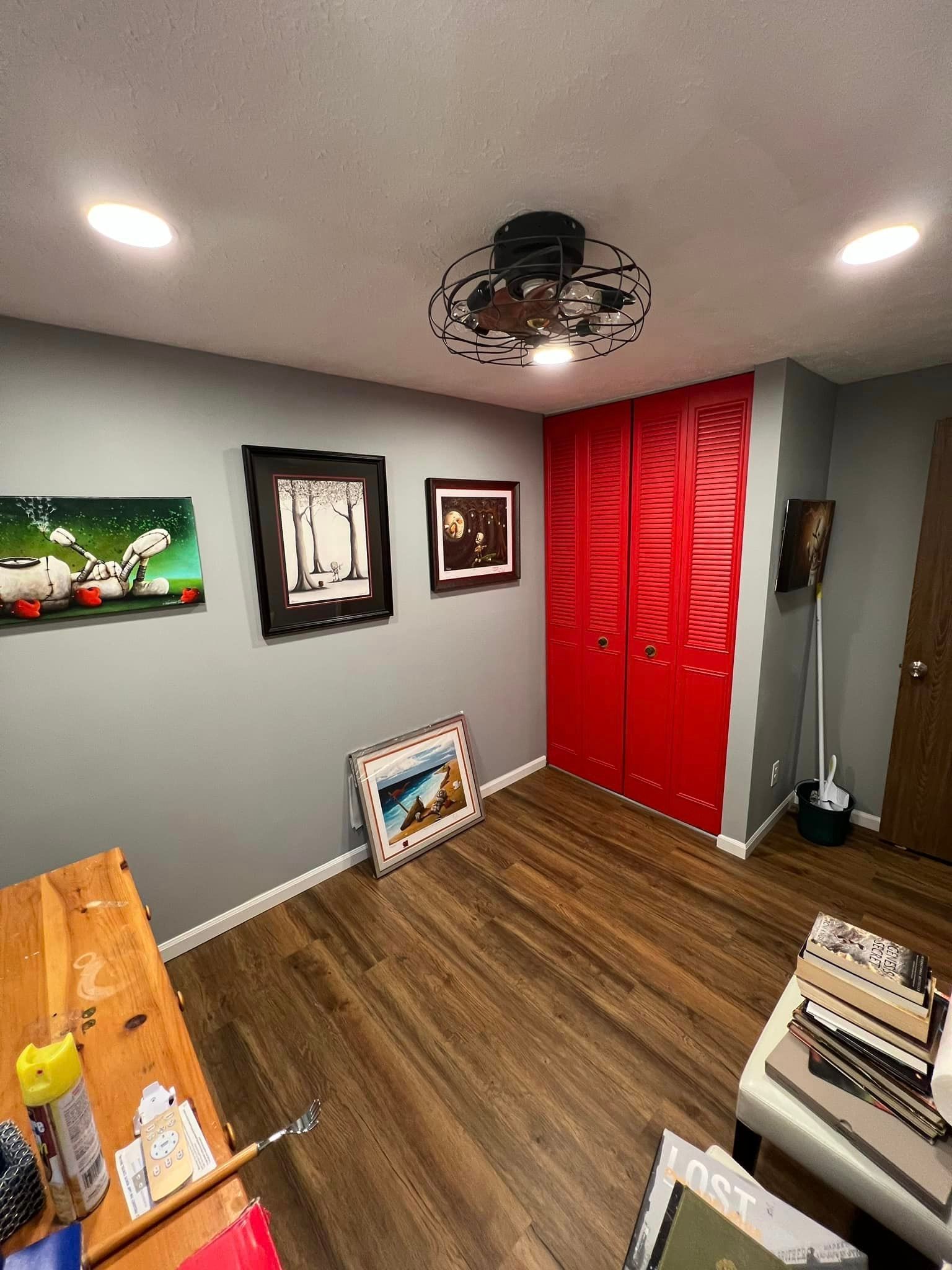 A room with a wooden floor , a ceiling fan , and red doors.