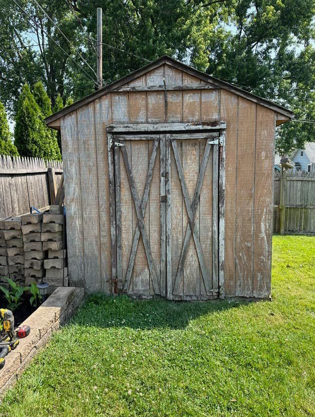 A wooden shed is sitting in the middle of a lush green yard.