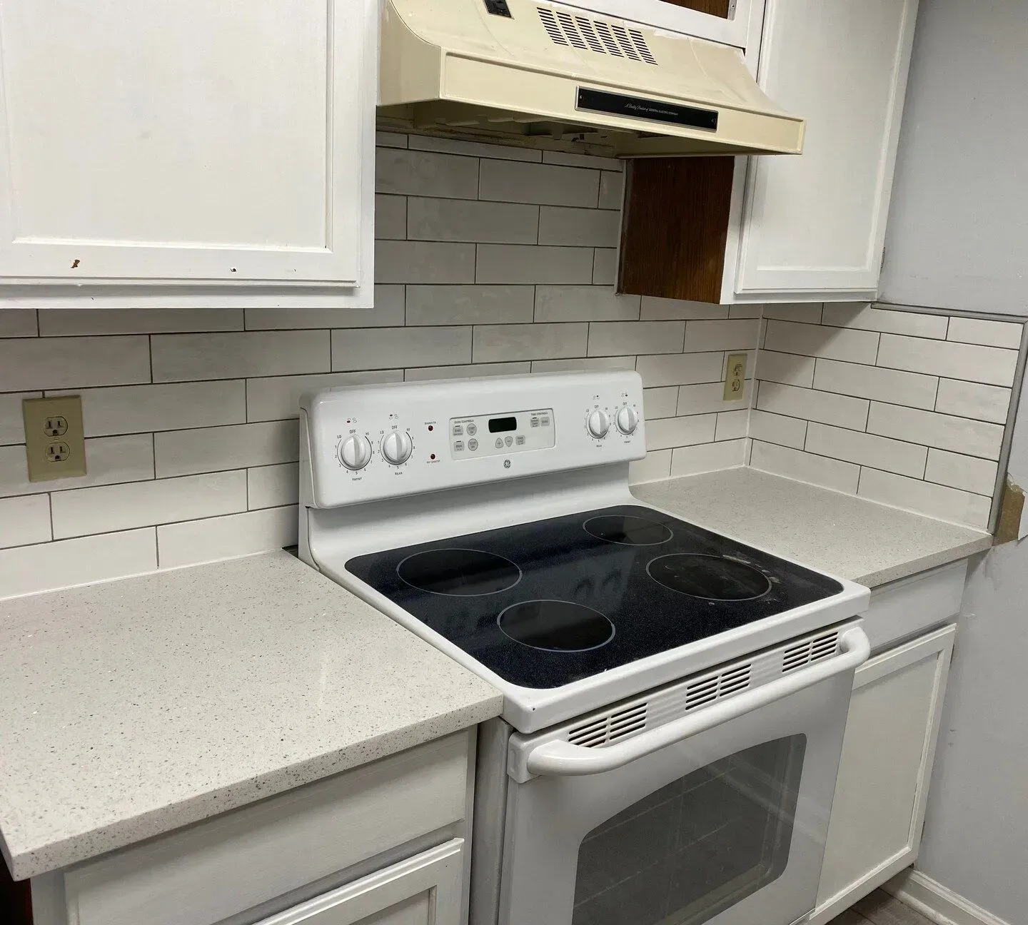 White kitchen with stove, countertops, cabinets, and a range hood against subway tile backsplash.