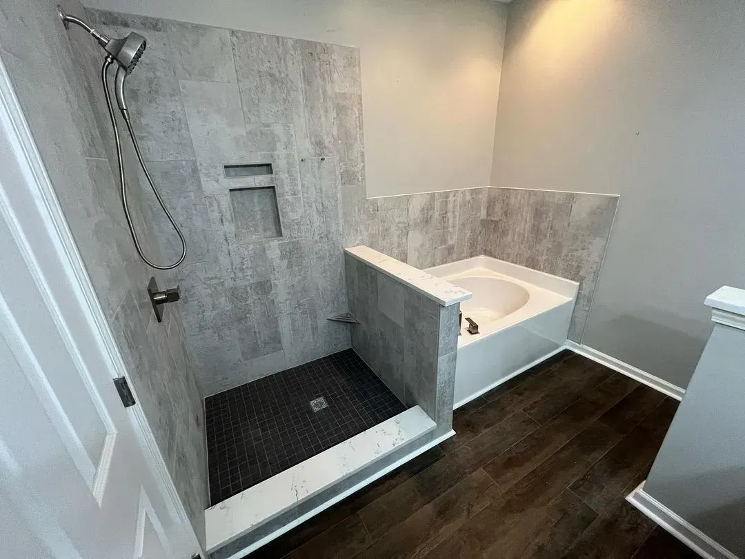 Bathroom with gray tiled shower and tub enclosure, dark wood floor, and white door.