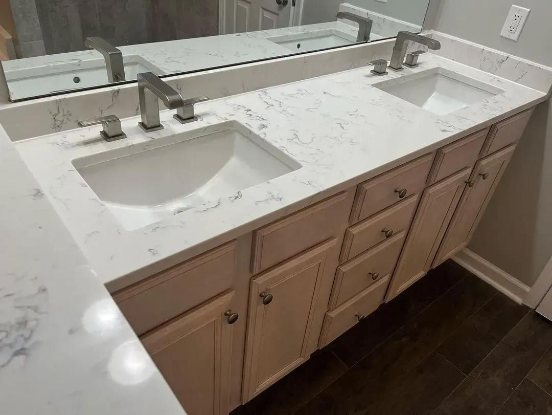 Bathroom vanity with two sinks, a white countertop with gray veining, and light-colored cabinets.