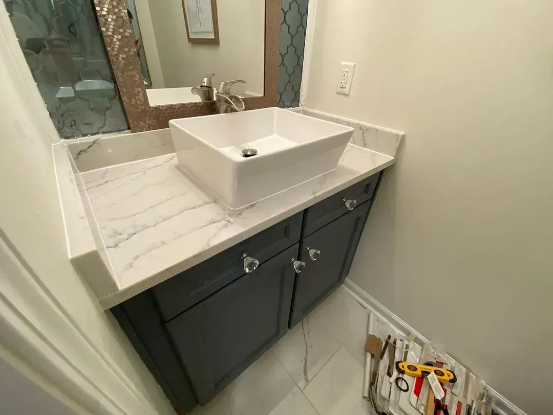 Bathroom vanity with white countertop, square sink, and blue-gray cabinet. Silver faucet, mirror, and crystal knobs.