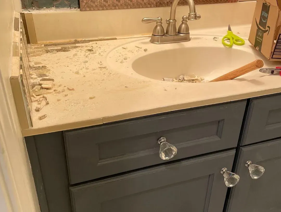Bathroom vanity under construction: light countertop, white sink, gray cabinets, crystal knobs, debris.