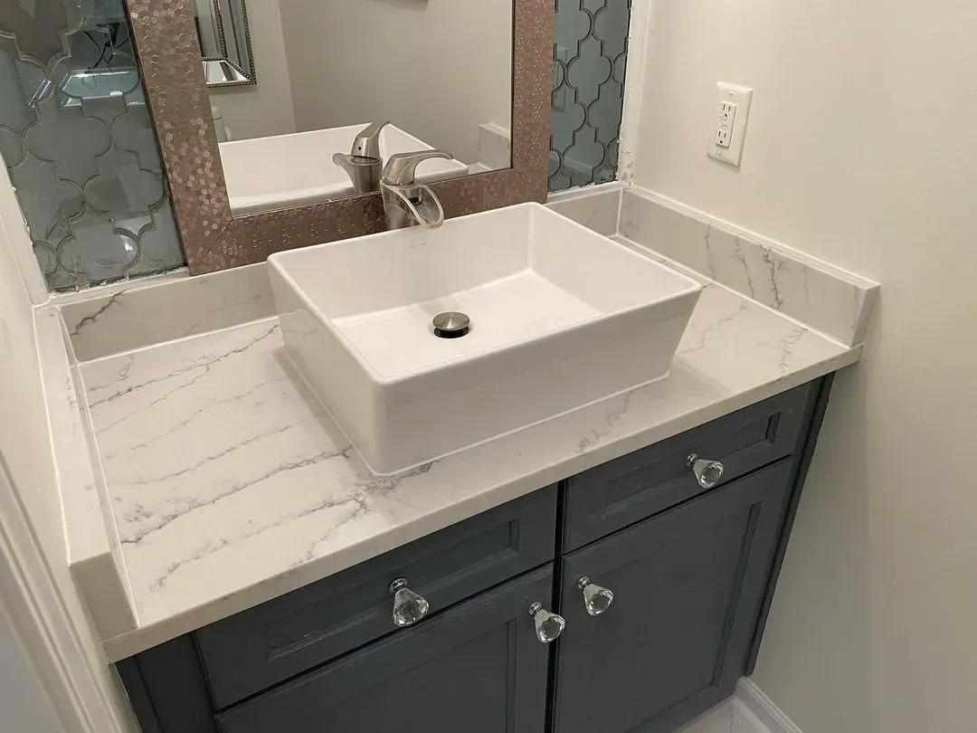 Bathroom vanity with square white sink, gray cabinets, and marble countertop.