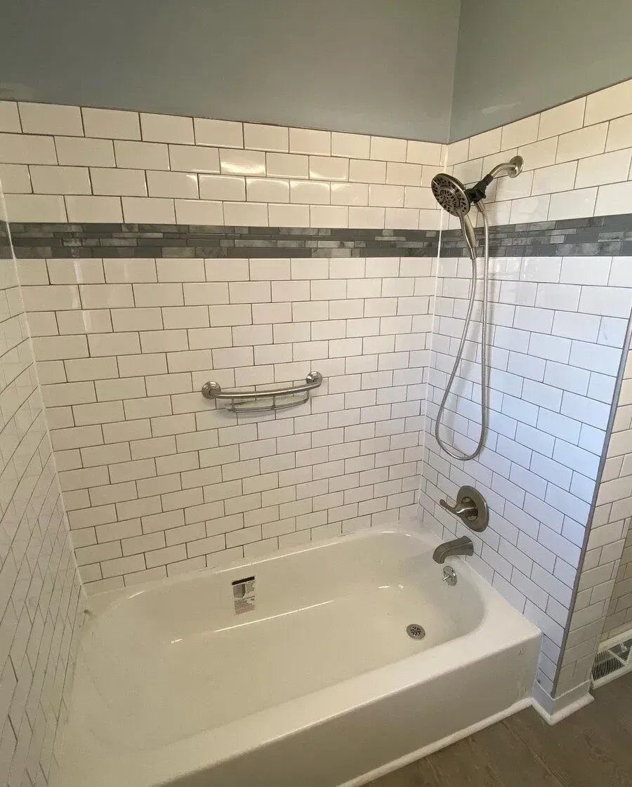 White tiled shower stall with bathtub, blue wall, gray accent tile.