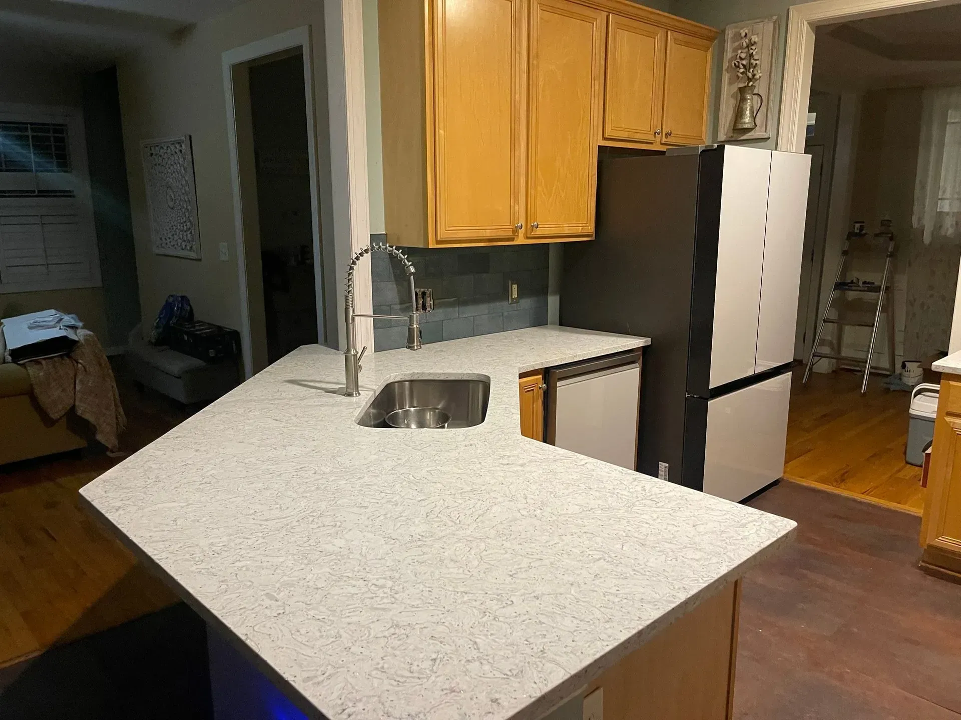 Kitchen with light quartz countertops, stainless steel sink and faucet, wooden cabinets, and a black and white refrigerator.