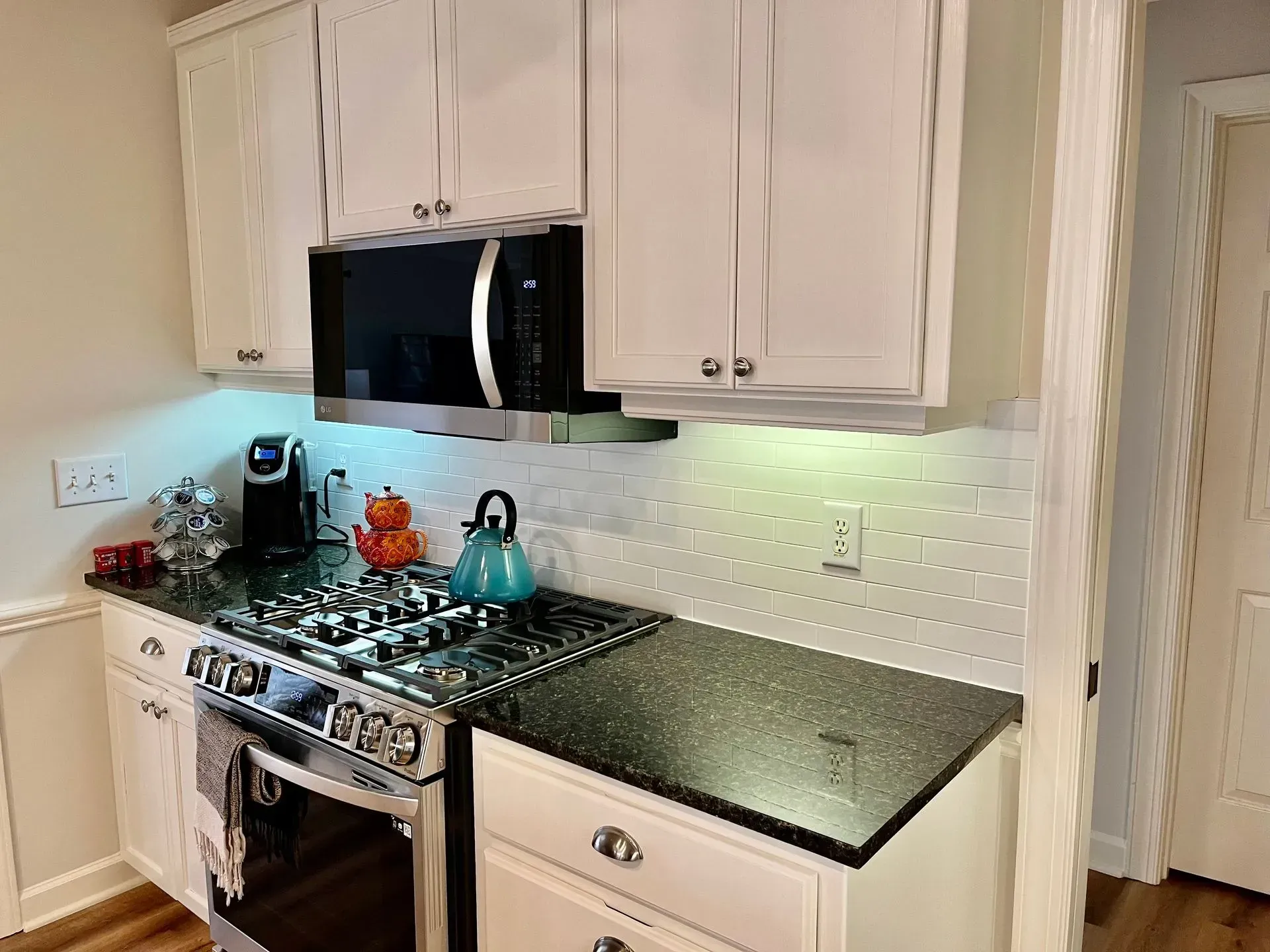 White kitchen with a black stovetop, microwave, and cabinets.