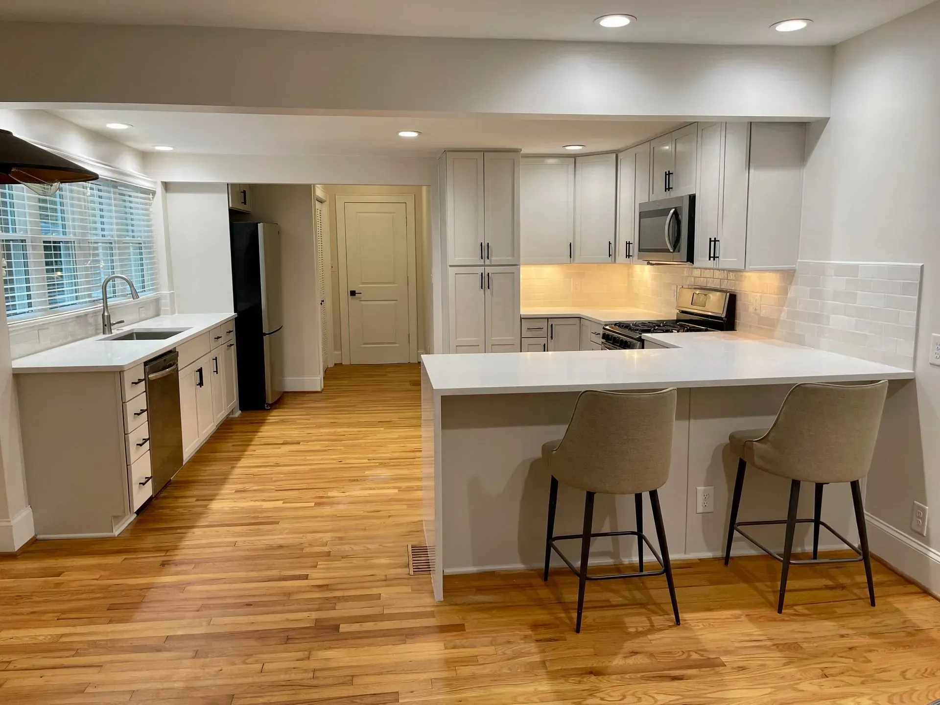 Modern white kitchen with island, wooden floors, and two bar stools.