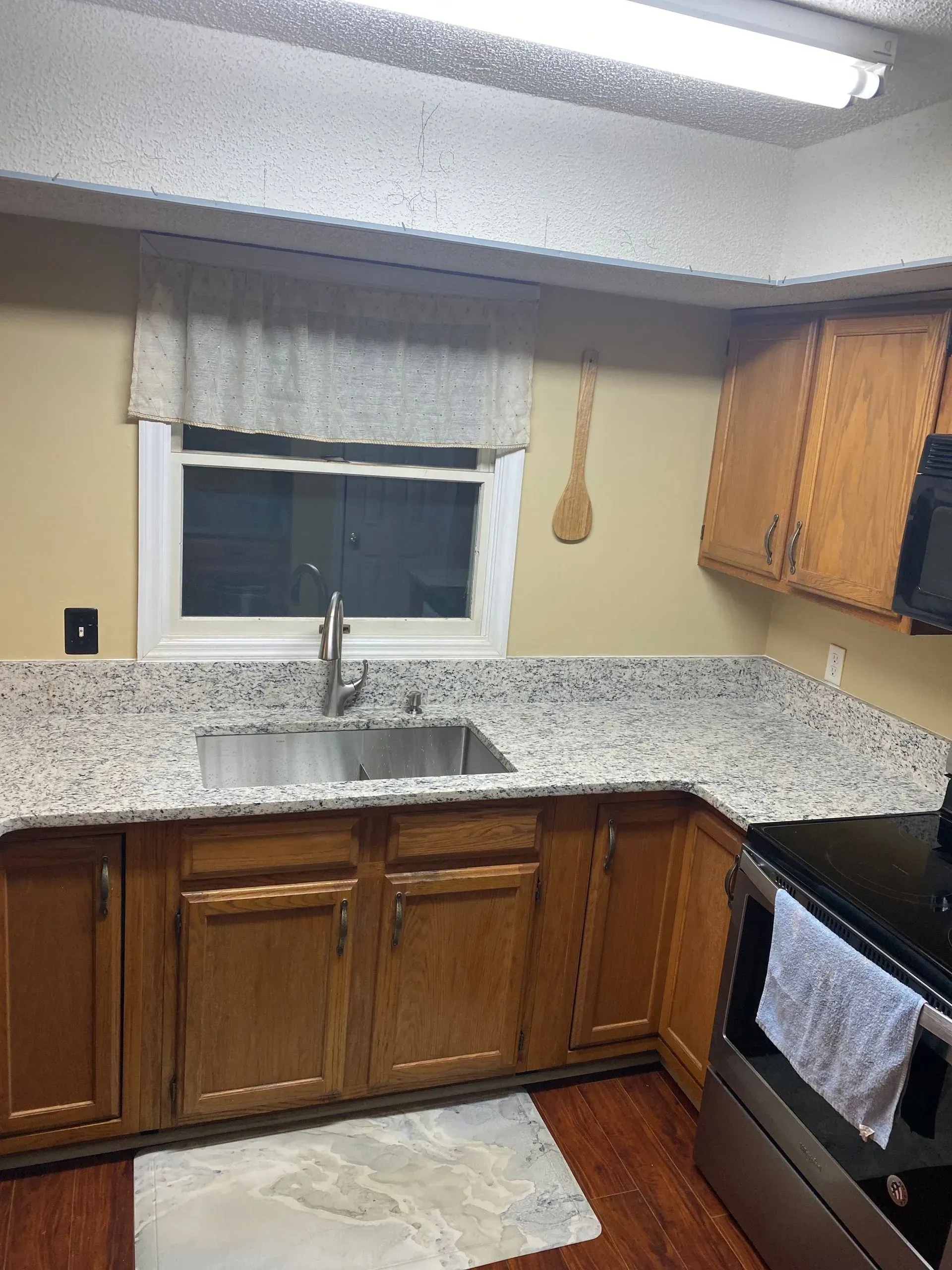 Kitchen with wooden cabinets, granite countertop, stainless steel sink, and a window with a valance.