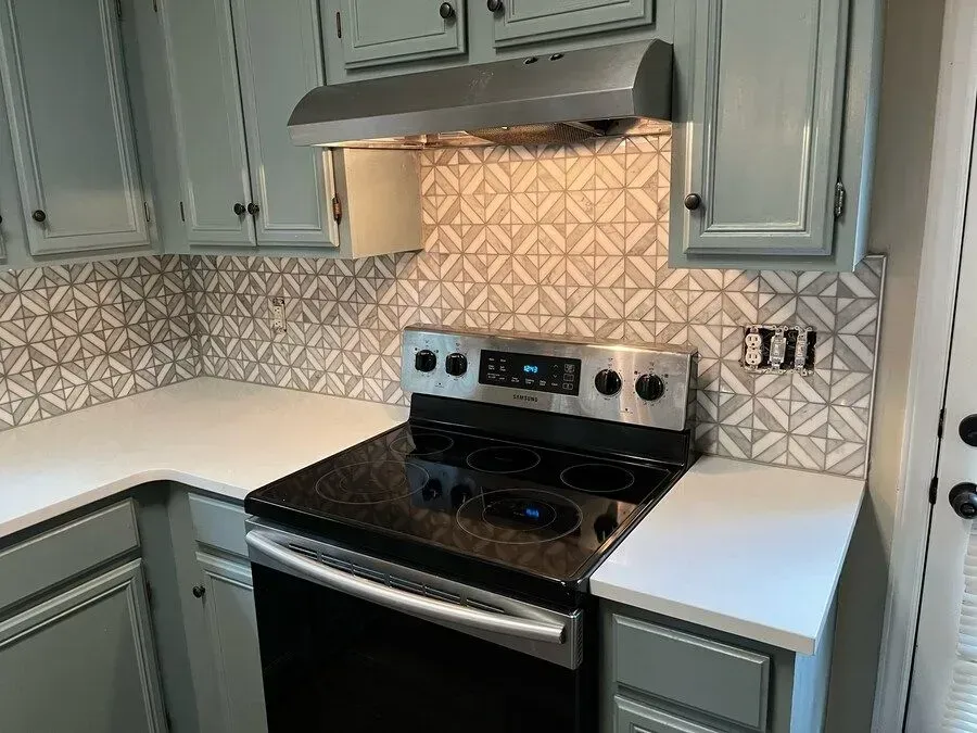 Kitchen with light blue cabinets, stainless steel range, patterned tile backsplash, and white countertops.