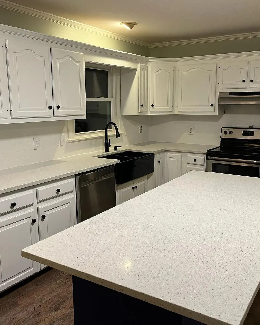 White kitchen with countertops and cabinets, stainless steel appliances, and a dark blue island.