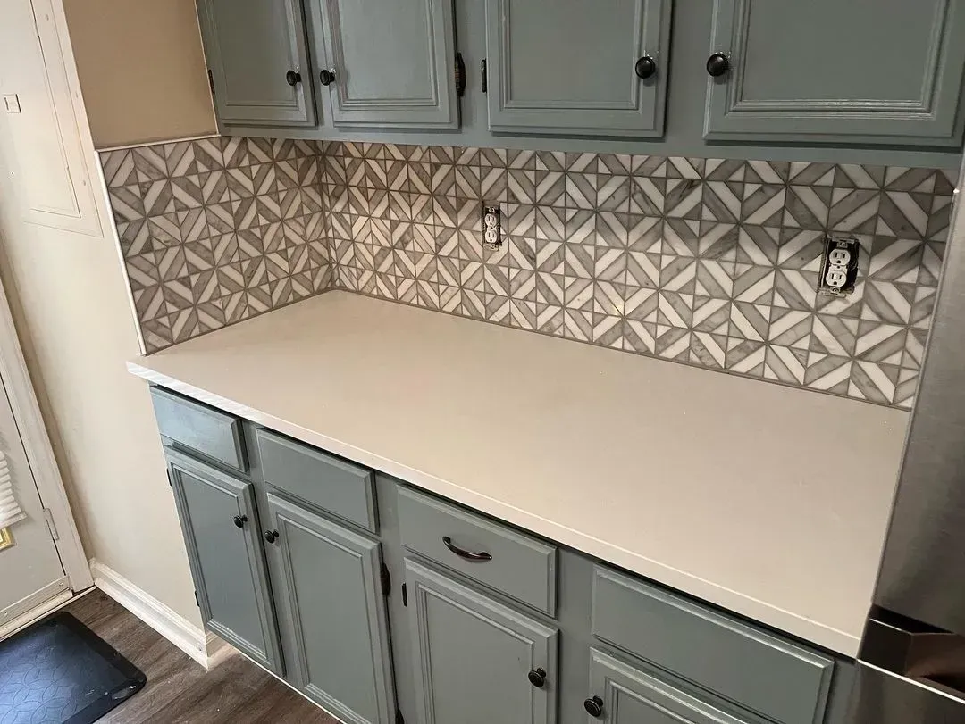 Gray kitchen with blue cabinets, white countertops, and patterned backsplash.