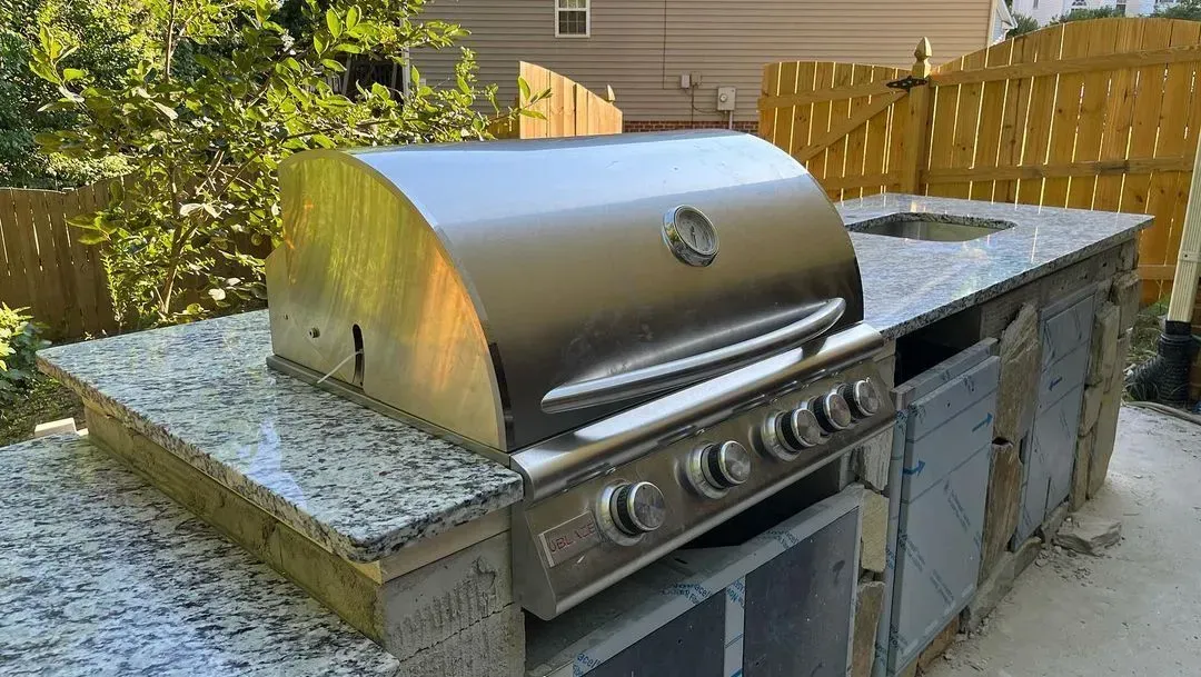 Outdoor kitchen with stainless steel grill, granite countertop, and stone facade.