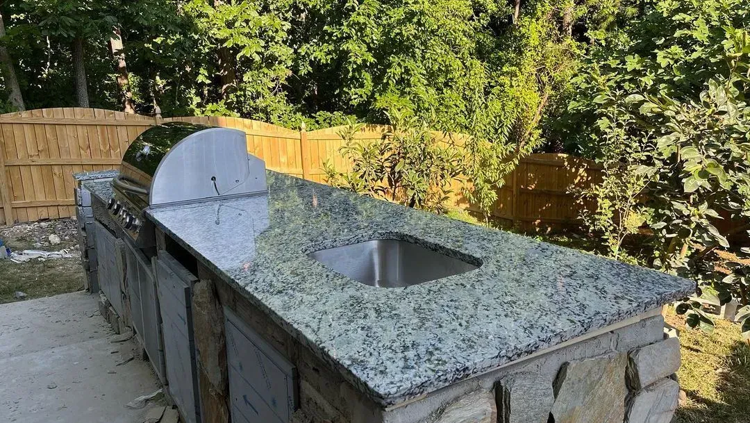 Outdoor kitchen with granite countertop, sink, grill, and stone base.