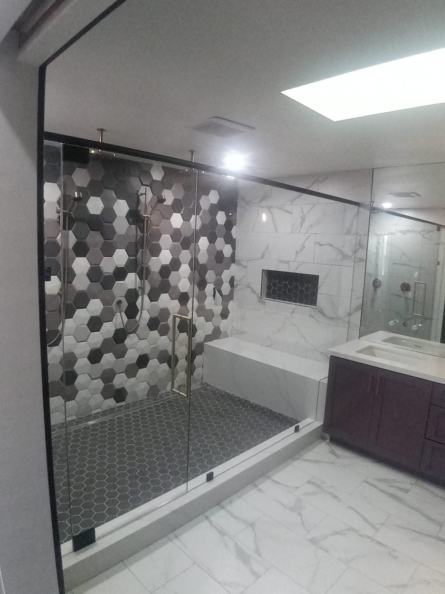 Modern bathroom with glass shower, patterned tile, and marble walls.