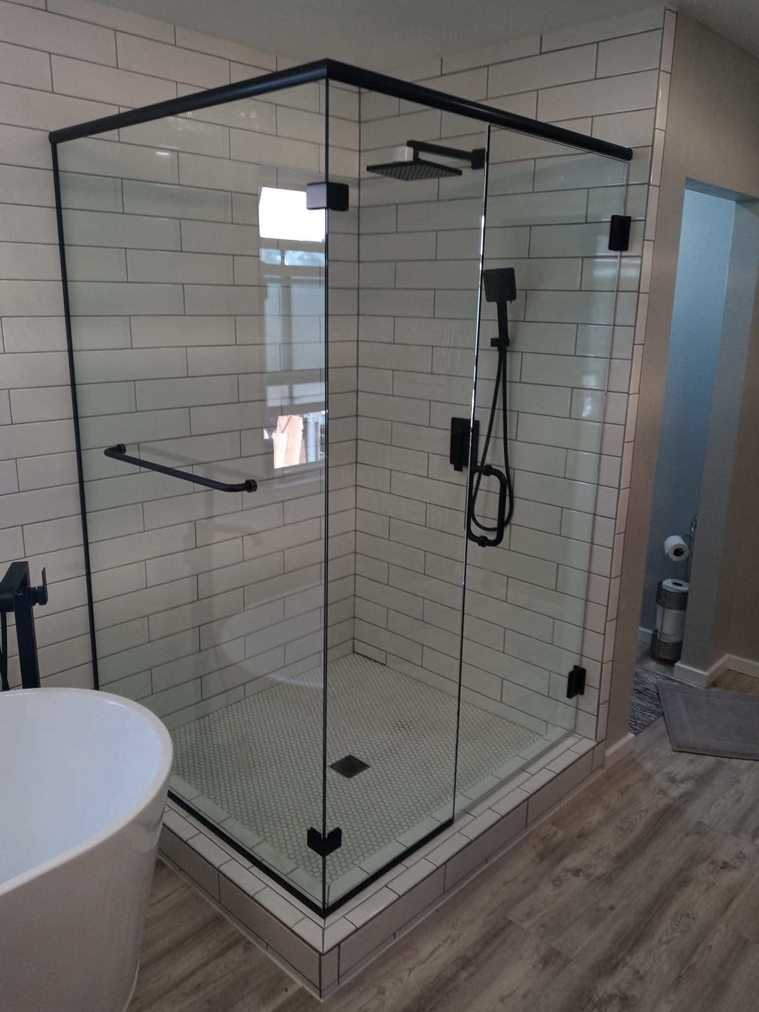 Modern glass shower enclosure with black hardware, white subway tile walls, and a gray tile floor.