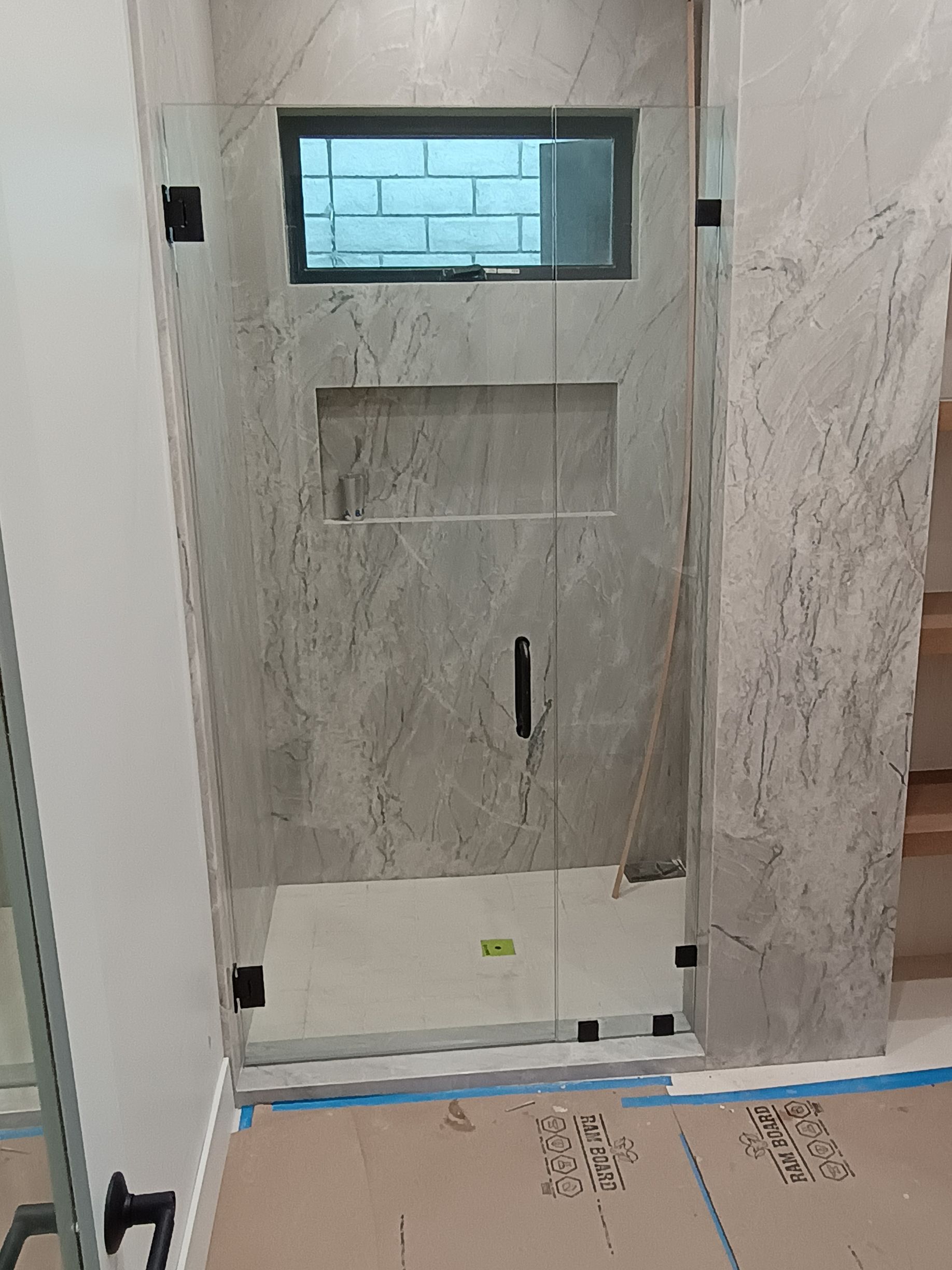 Glass shower enclosure with black hardware, marble-like tiled walls, and small window.
