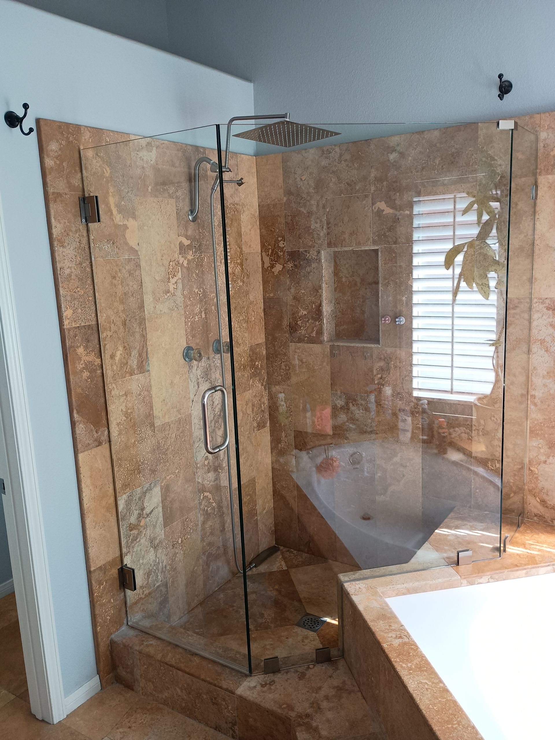 Glass shower enclosure with brown stone tile walls, next to a bathtub.