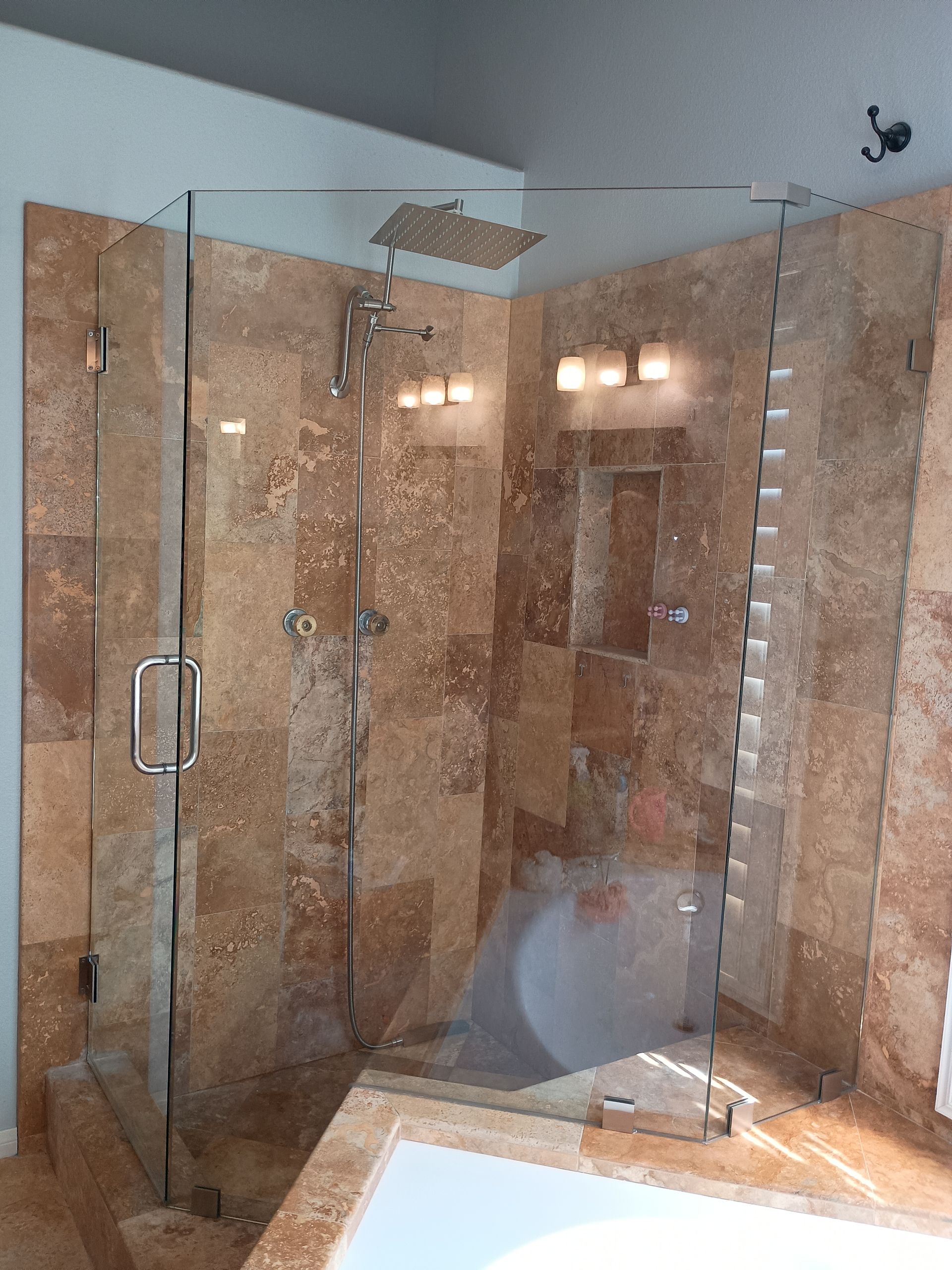Corner shower enclosure with glass doors and travertine tile.