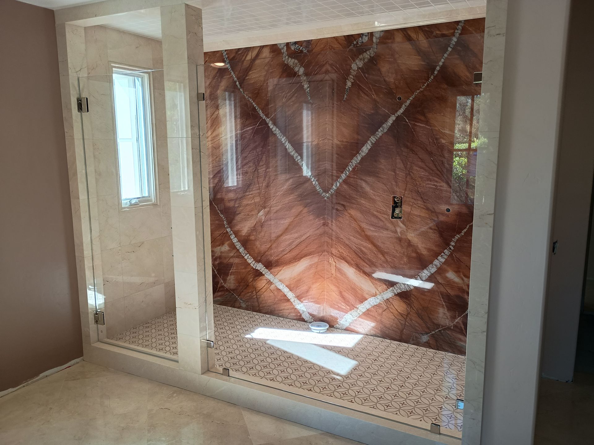 Two-stall shower with glass doors and reddish-brown wall. Both stalls have a small stone floor.