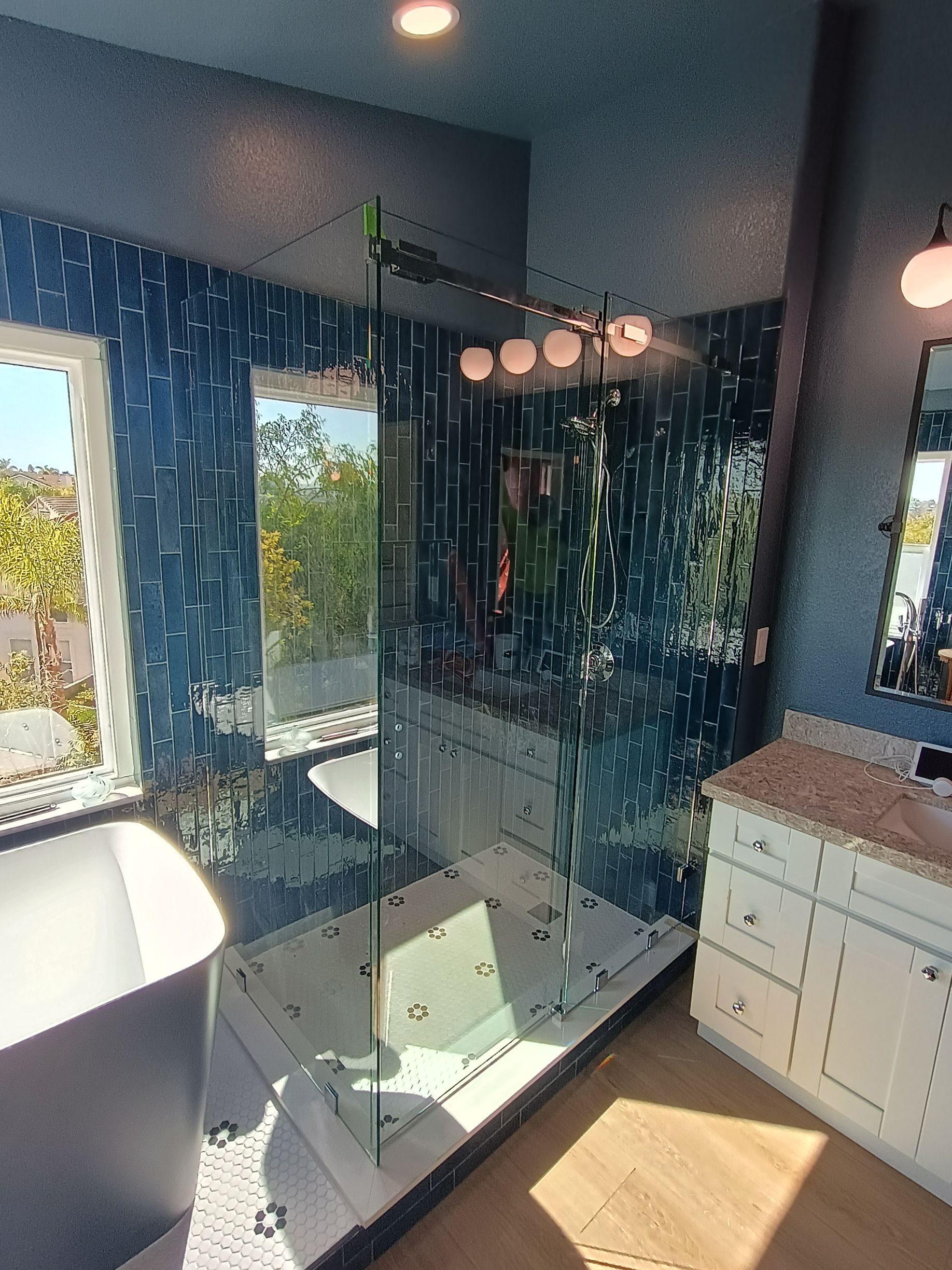 Modern bathroom with blue mosaic tiles, a glass shower, vanity, and a freestanding tub.