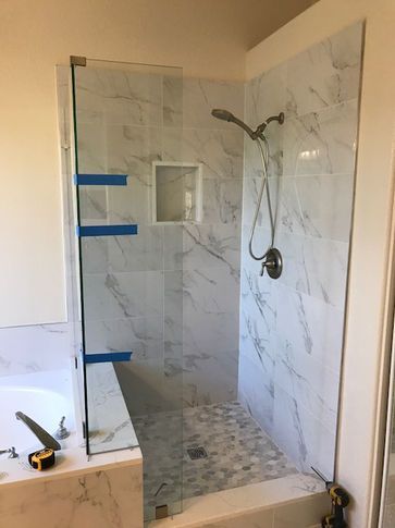 Shower with white marble tile walls, glass door, and pebble floor. Blue tape marks glass placement.