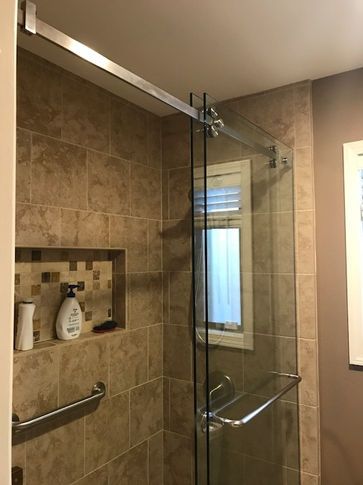 Glass shower enclosure with sliding door and a built-in shelf in a tiled shower.