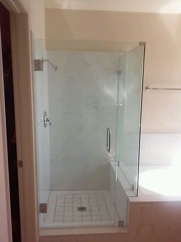 Glass shower enclosure with white tile floor and marble wall.