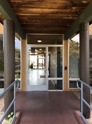 Exterior building entrance with glass doors, brown columns, and a ramp.