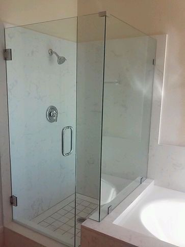 Glass shower enclosure with white marble walls and a chrome showerhead and fixtures.