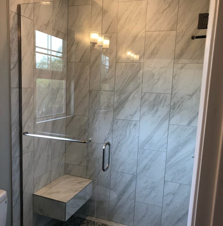 Modern tiled shower with glass door and built-in bench.