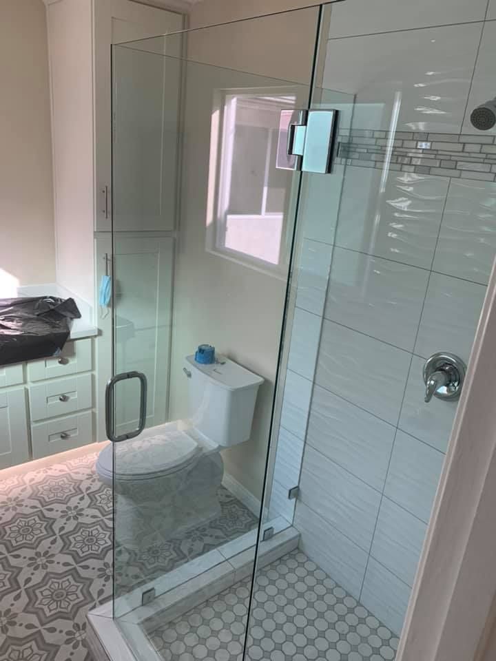 Bathroom with glass shower door, white tiles, toilet, cabinet, patterned floor, and window.