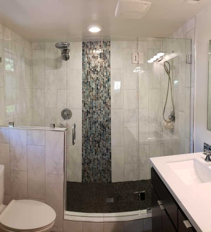Modern bathroom with tiled shower, glass door, dark vanity, and toilet.