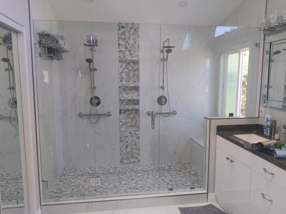 Spacious, modern shower with glass doors, two shower heads, grab bars, and pebble floor.