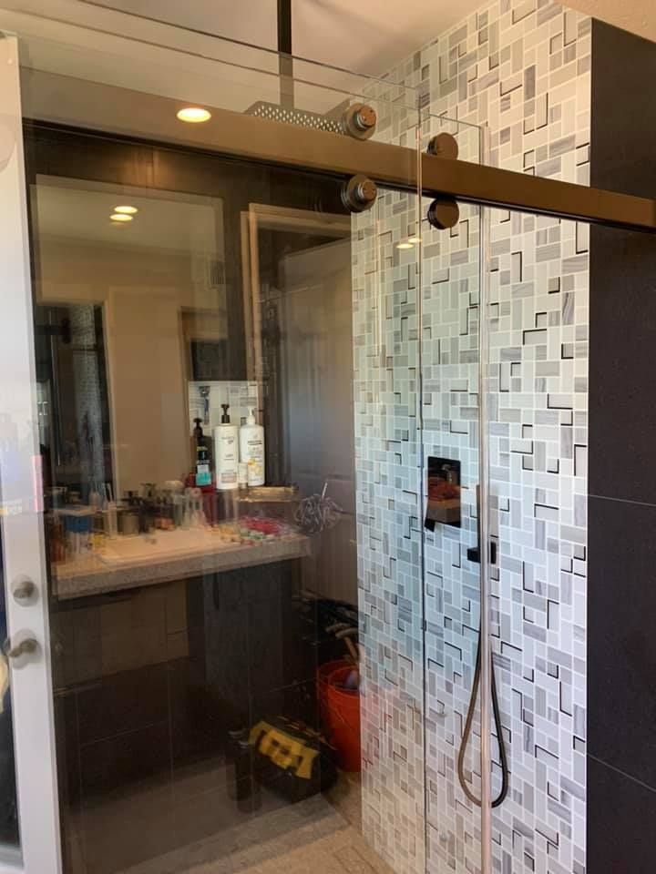 Glass shower with sliding door and decorative tile wall. Black hardware and fixtures.