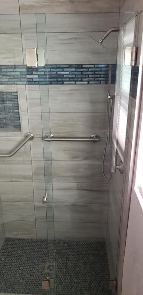 A tiled shower with a glass door, showerhead, and a mosaic floor.