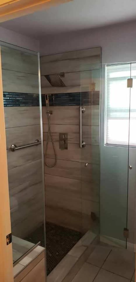 A modern shower with glass walls and a tiled interior, a window on the right.