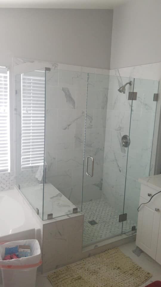 Modern bathroom with glass shower enclosure, marble walls, and white cabinets.