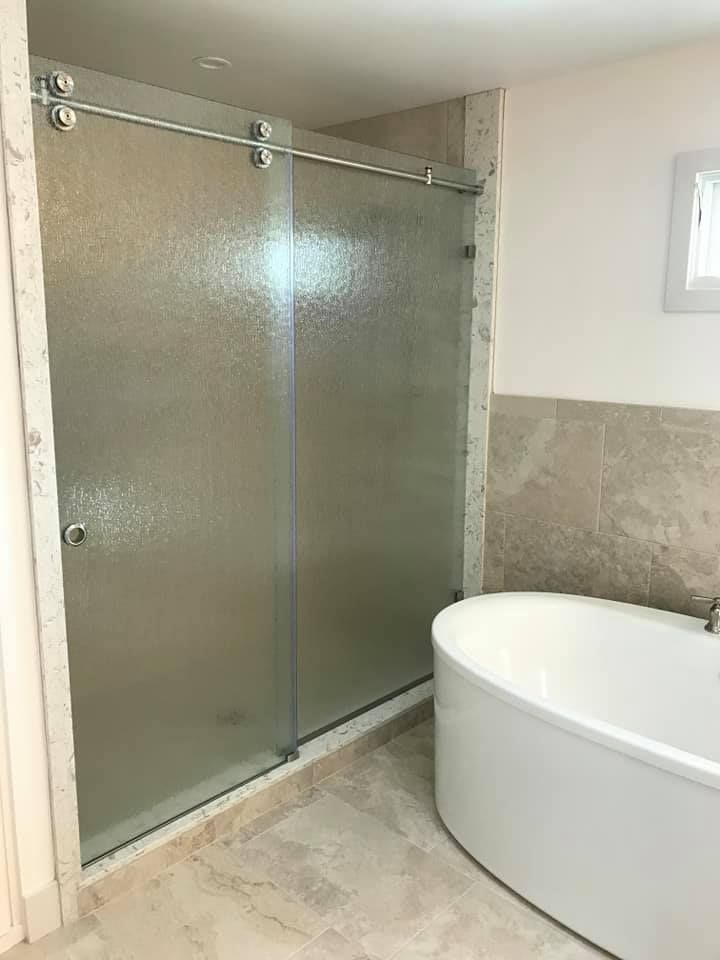 Sliding glass shower door with textured glass in a bathroom, next to a white bathtub.