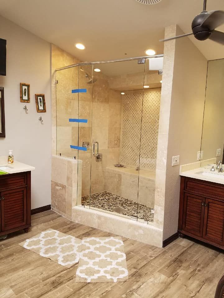 A luxurious bathroom with a glass shower, dark wood cabinets, and light stone tile. Two ornate rugs on the floor.