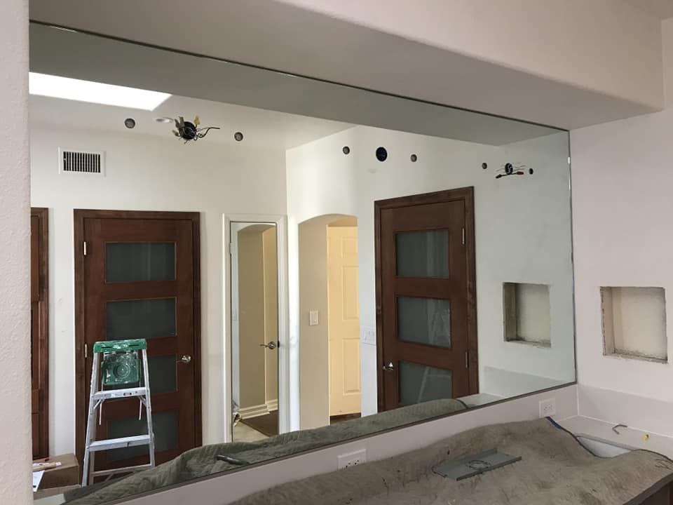 Large rectangular mirror installed on a wall, reflecting interior with doors and a ladder.
