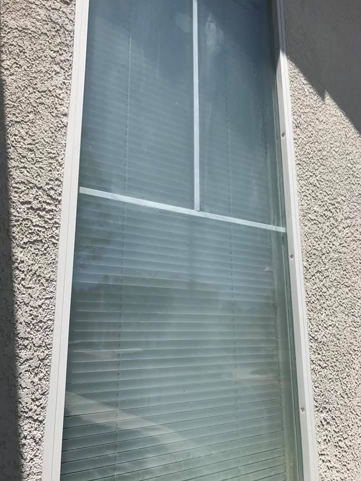 Tall white window on textured light gray stucco wall, with horizontal blinds visible through the glass.